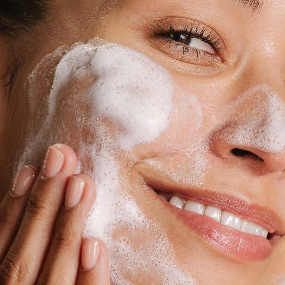 Close-up of a woman applying breakout clearing foaming wash to her face.