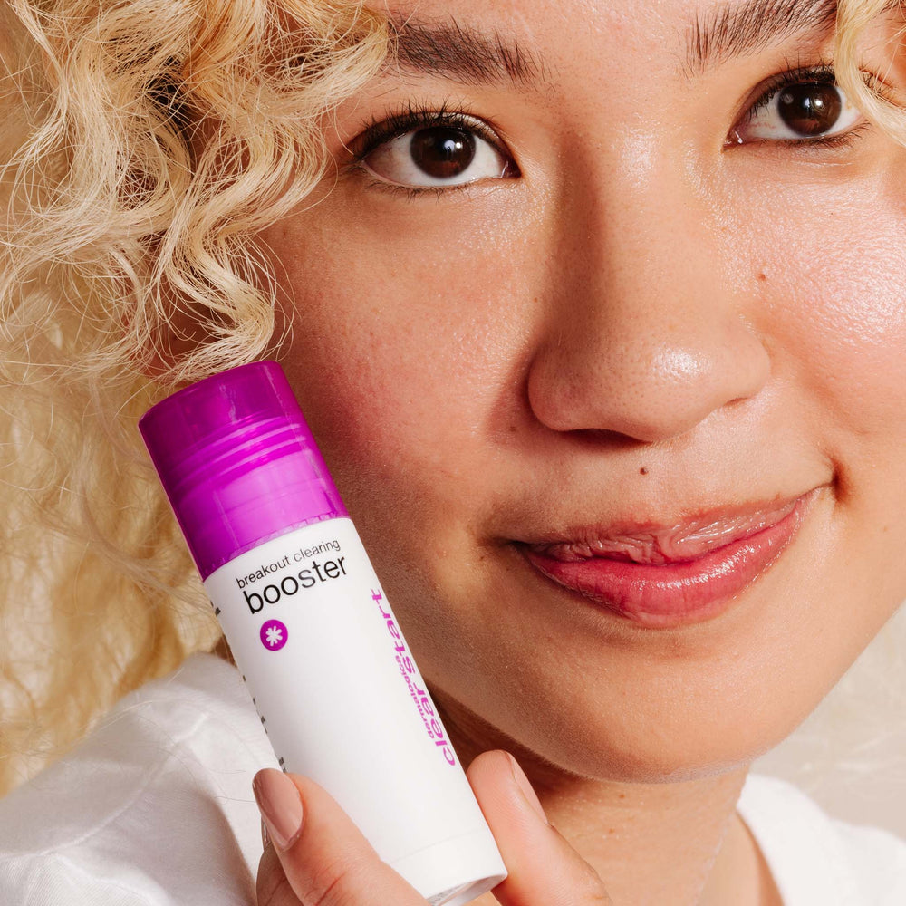 Person holding a 'breakout clearing booster' product close to their face
