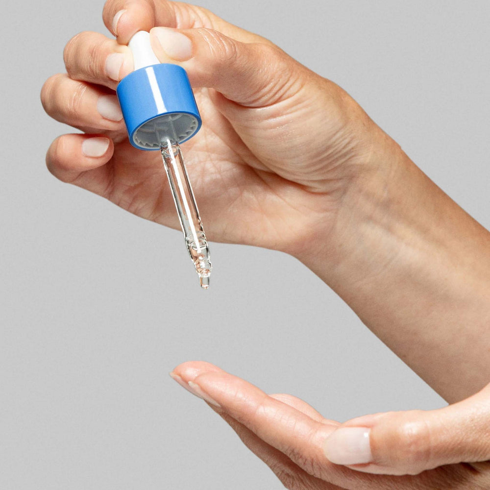 Hand holding a circular hydration serum dropper against a gray background